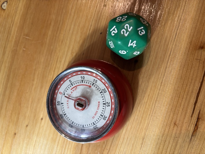 A 30-sided die and a red Kikkerland kitchen timer on a wooden table